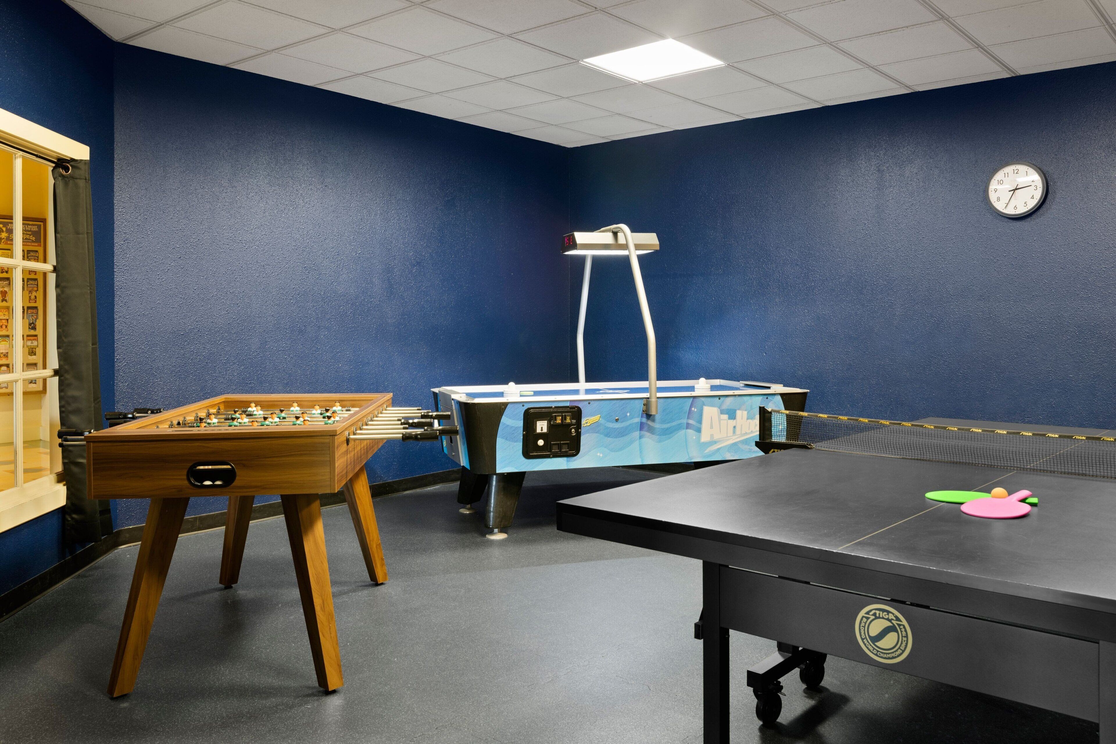 A room with a foosball table, a pool table, and a clock on the wall.