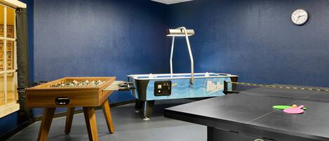 A room with a foosball table, a pool table, and a clock on the wall.