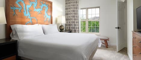 A bedroom with a large bed, a wooden headboard with a blue design, a bedside table with a lamp, a window with a view, and a TV on the right.
