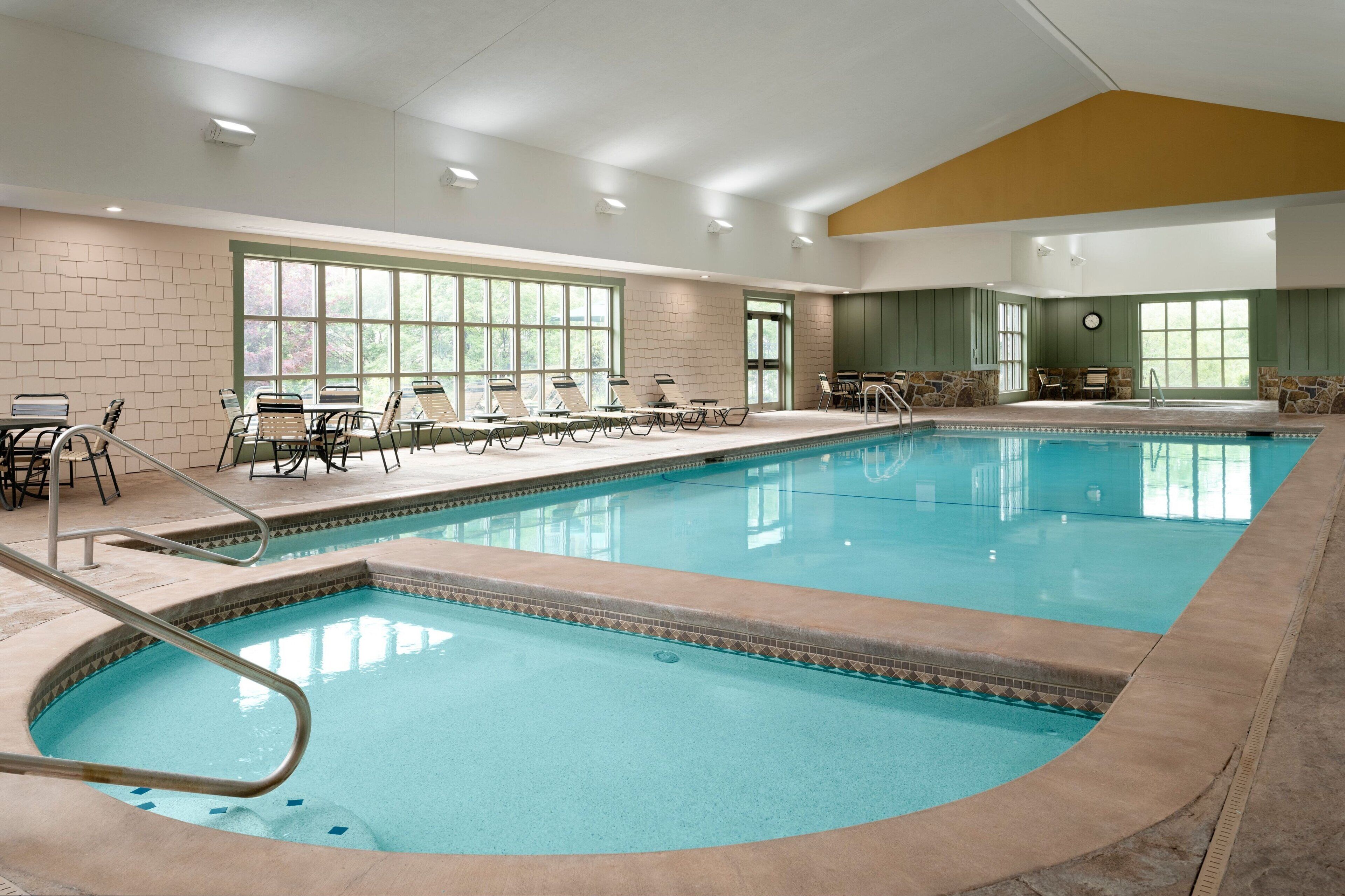An indoor swimming pool with multiple lanes, lounge chairs, and tables along the sides.