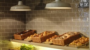 Una exhibición de panadería con panes y pasteles varios en cestas de mimbre, iluminada por luces colgantes.