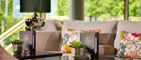 A modern living area with a sofa, a glass-top coffee table, and a lamp. There are two potted plants on the table.