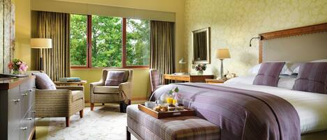 Une chambre d’hôtel avec un grand lit, un coin salon comprenant un fauteuil et une petite table, une commode et une fenêtre avec des rideaux.