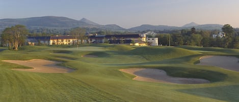 A golf course with bunkers, a clubhouse, and distant mountains.
