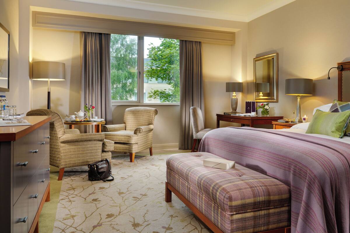 A hotel room with a bed, a chair, a desk, and a window with curtains.