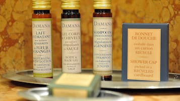 Three bottles of Damana body care products and a cardboard box labeled "BONNET DE DOUCHE" on a tray.