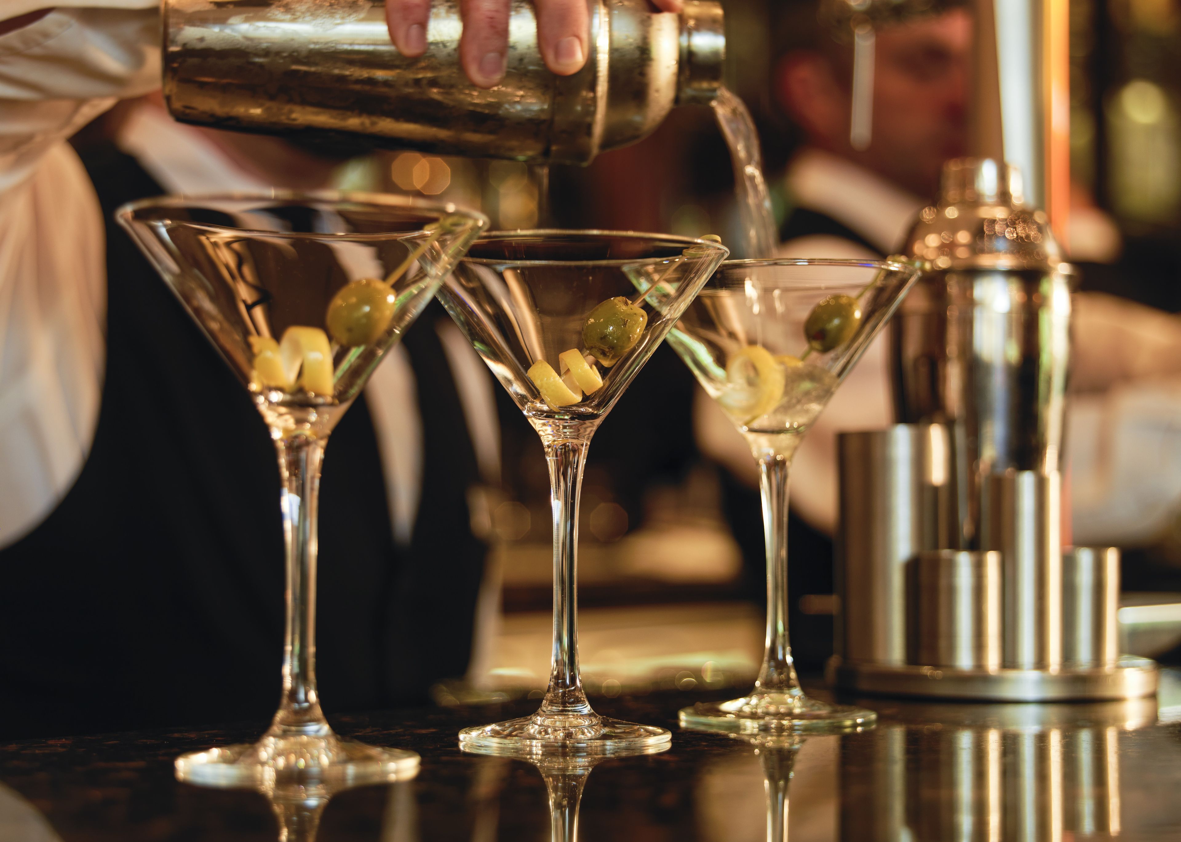 A bartender pouring a drink into a martini glass.