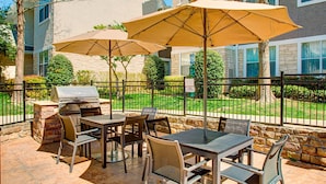 An outdoor patio with a grill, tables, chairs, and umbrellas. - Residence Inn By Marriott Dallas Park Central (Dallas)