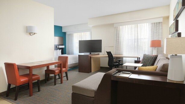 A hotel room with a desk, a sofa, a TV, and a lamp. - Residence Inn By Marriott Dallas Park Central (Dallas)