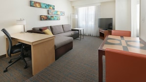 A hotel room with a desk, a sofa, a television, and artwork on the wall. - Residence Inn By Marriott Dallas Park Central (Dallas)