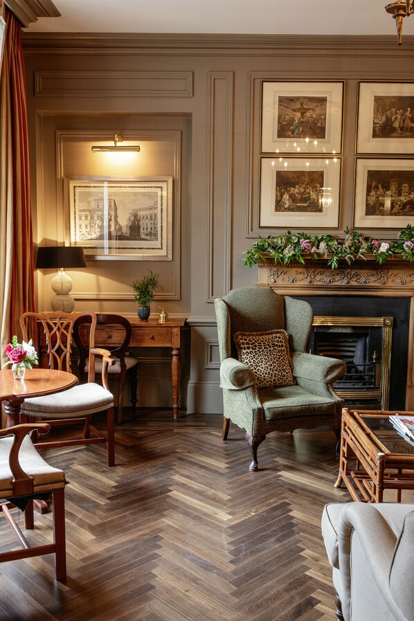 A room with a fireplace, framed pictures on the wall, a dining table with chairs, and a sofa.