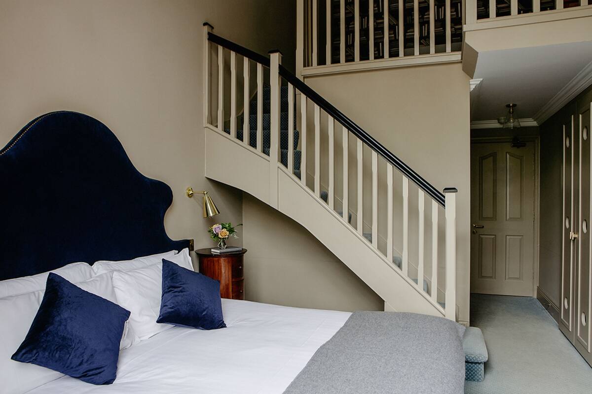 A bedroom with a bed, pillows, a nightstand, and a staircase.