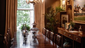 A dining room with a long wooden table, chairs, a chandelier, and a window with curtains. - Pembroke Townhouse (Dublin)