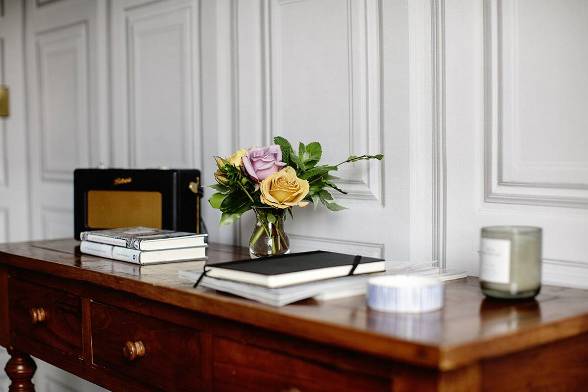A wooden desk with a book, a vase with flowers, and a candle.