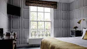 A room with a large window, a bed with a gold throw, a desk with a computer, and a TV mounted on the wall. - Pembroke Townhouse (Dublin)