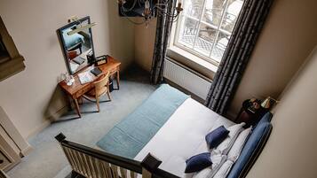A hotel room with a bed, a desk with a chair, a mirror, and a window with curtains.