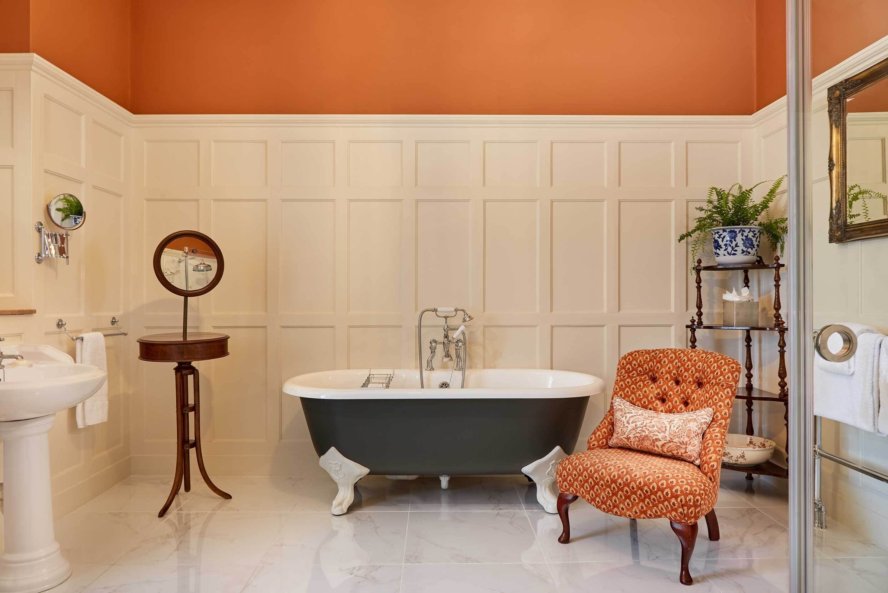 A bathroom with a freestanding bathtub, a pedestal sink, a vanity with a mirror, and a chair.