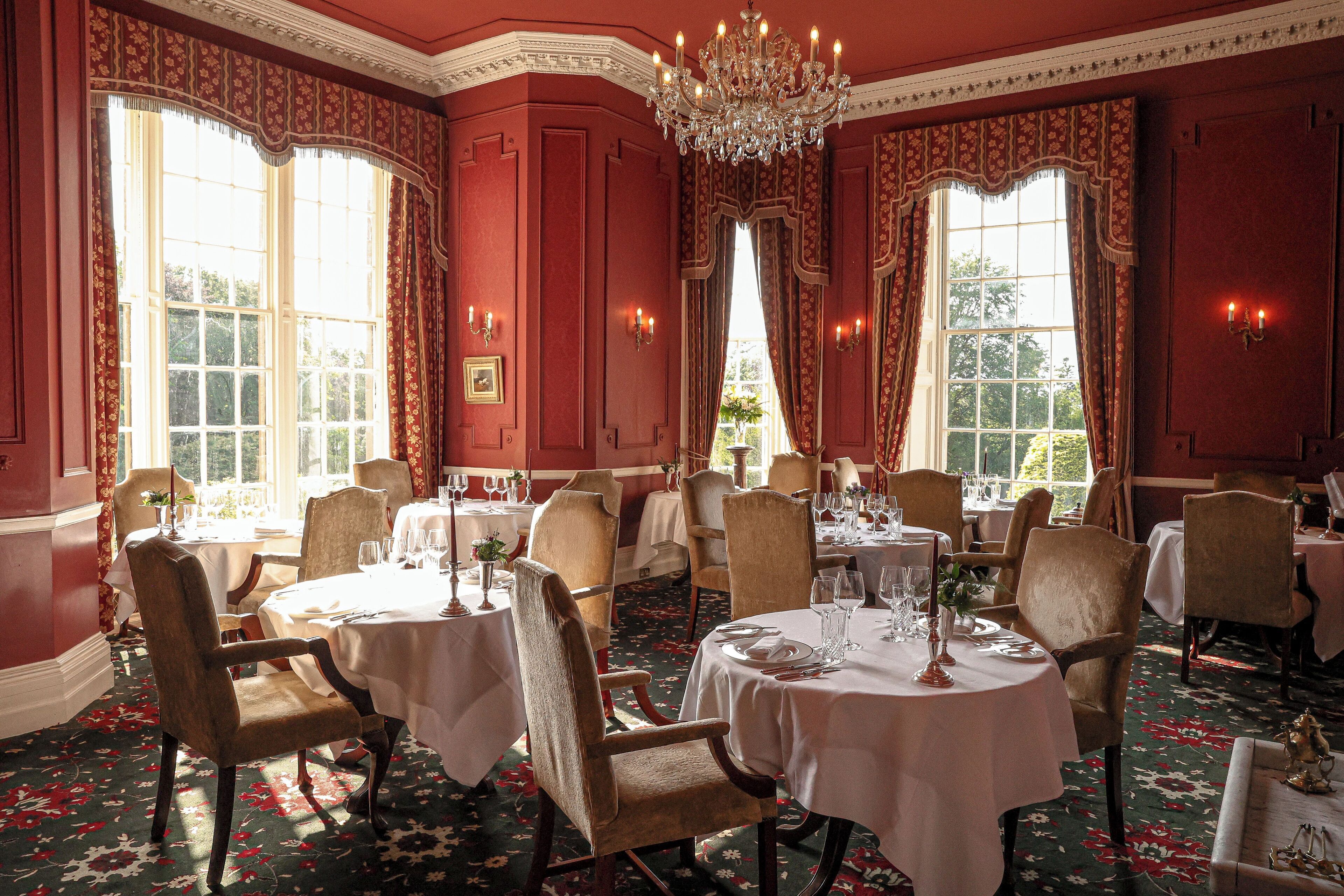 A formal dining room with multiple round tables, elegant chairs, and chandeliers.