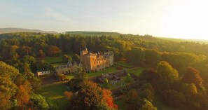 Um castelo rodeado por uma paisagem verdejante e exuberante, com um jardim bem cuidado e céu claro.
