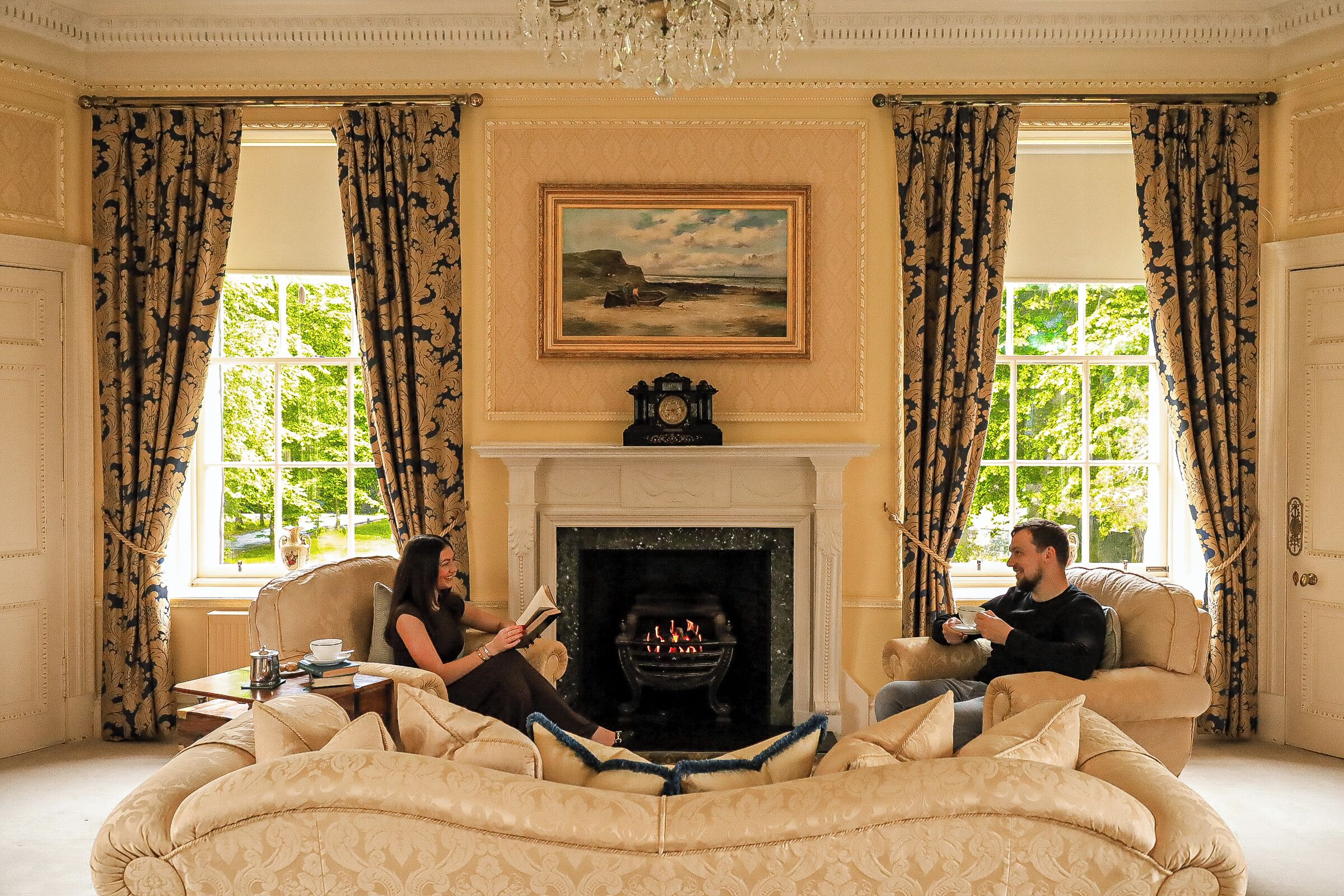 A room with a fireplace, two sofas, a table with a book and a teapot, and a painting above the fireplace.