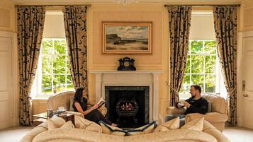 A room with a fireplace, two sofas, a table with a book and a teapot, and a painting above the fireplace.