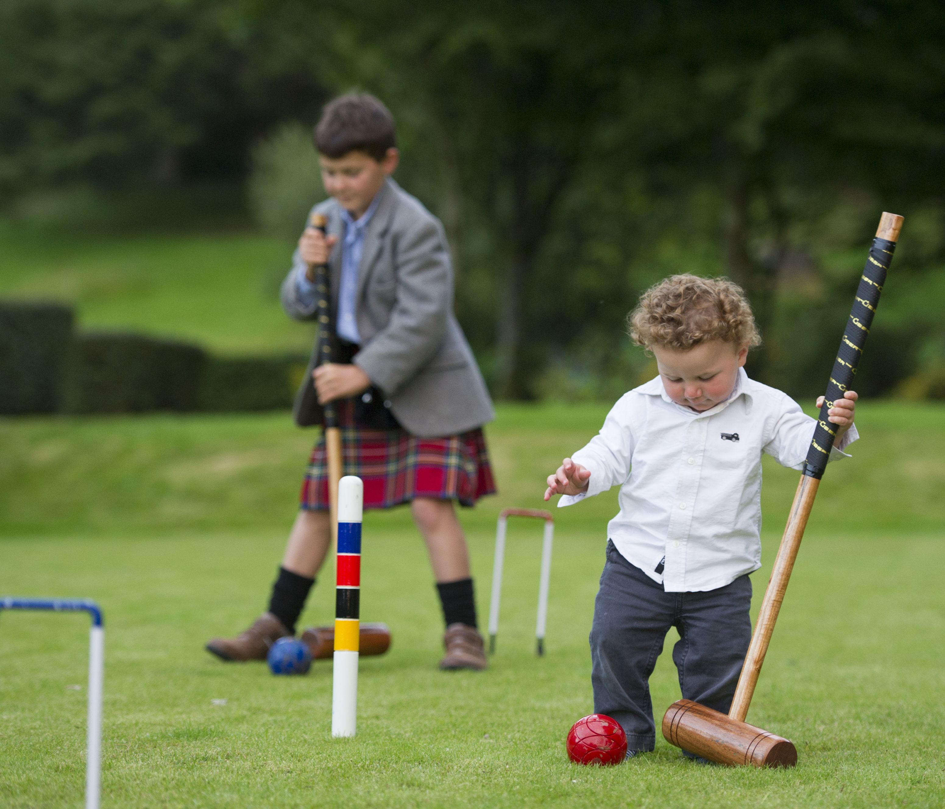 Crianças brincando de croquet num campo gramado.