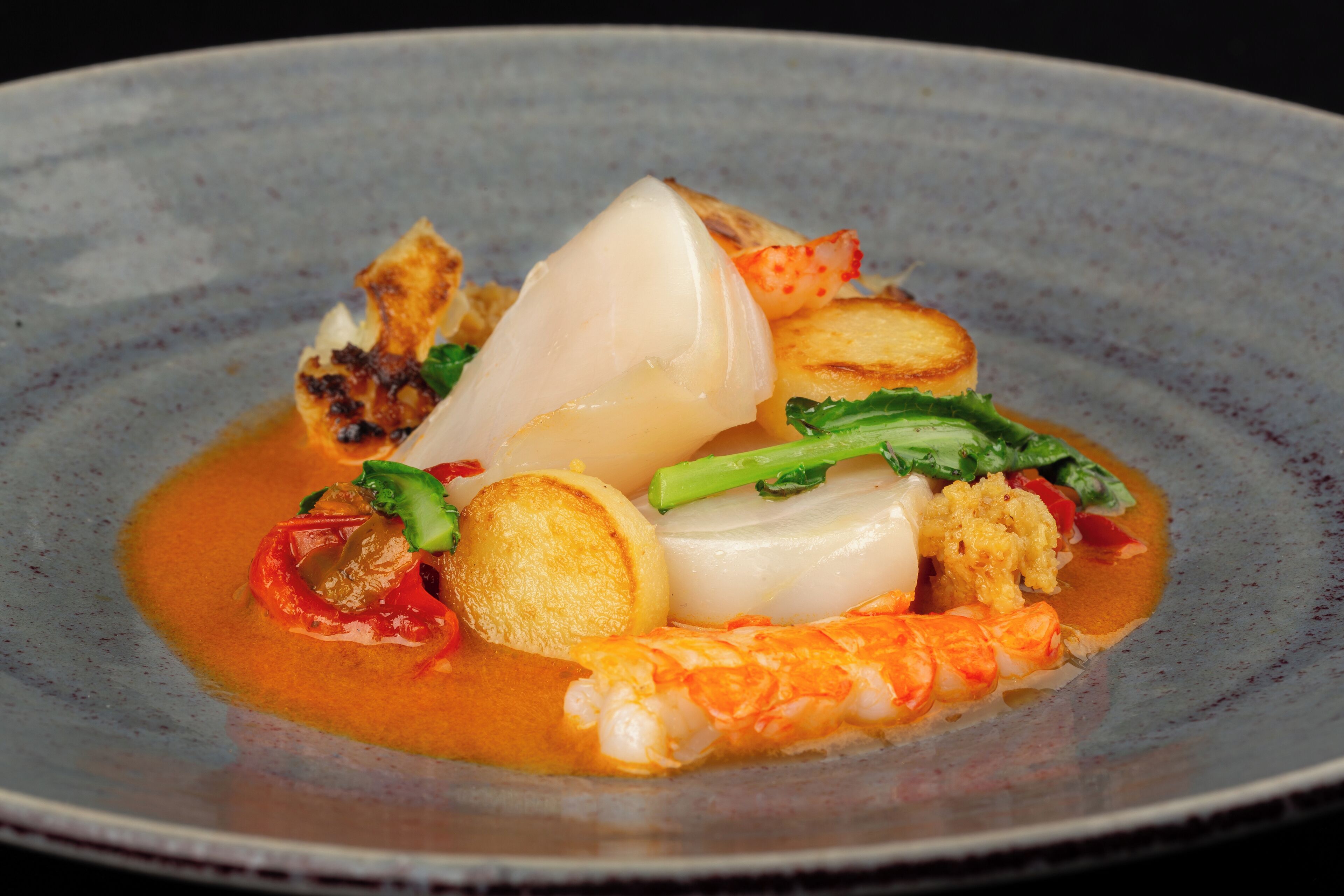 A plate of food with various ingredients including seafood, vegetables, and a sauce.