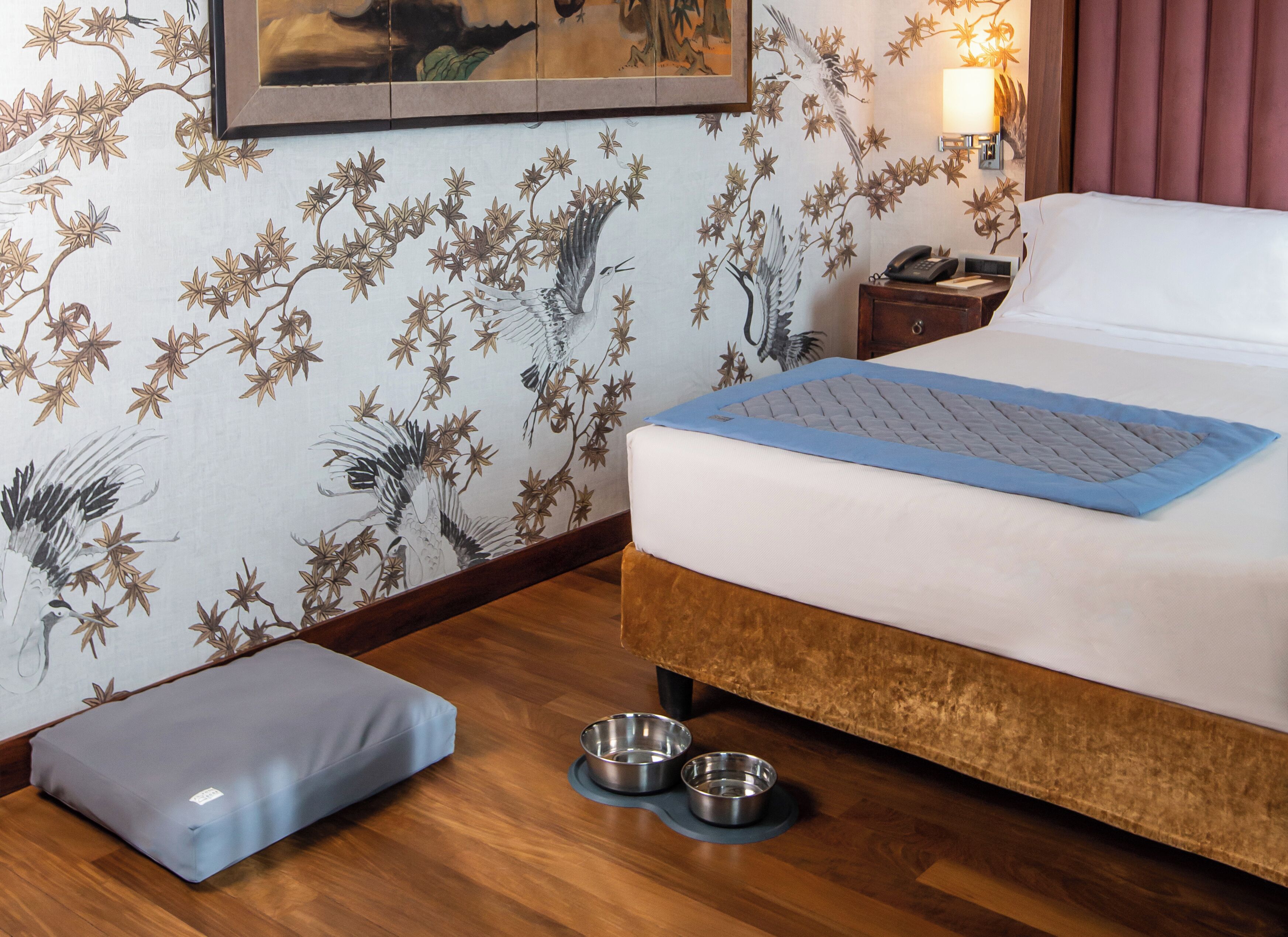 Une chambre d’hôtel avec un lit, une table de chevet, une lampe, une œuvre d’art encadrée au mur et un plancher en bois.