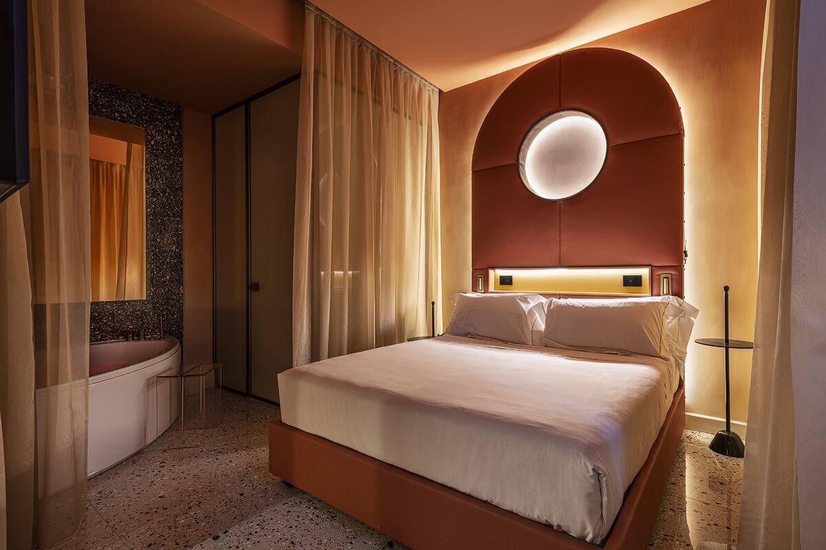 A hotel room with a bed, a bathroom, and a round light fixture on the wall.