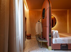 A modern hotel room with a unique curved bed, a round mirror, and a small round table.