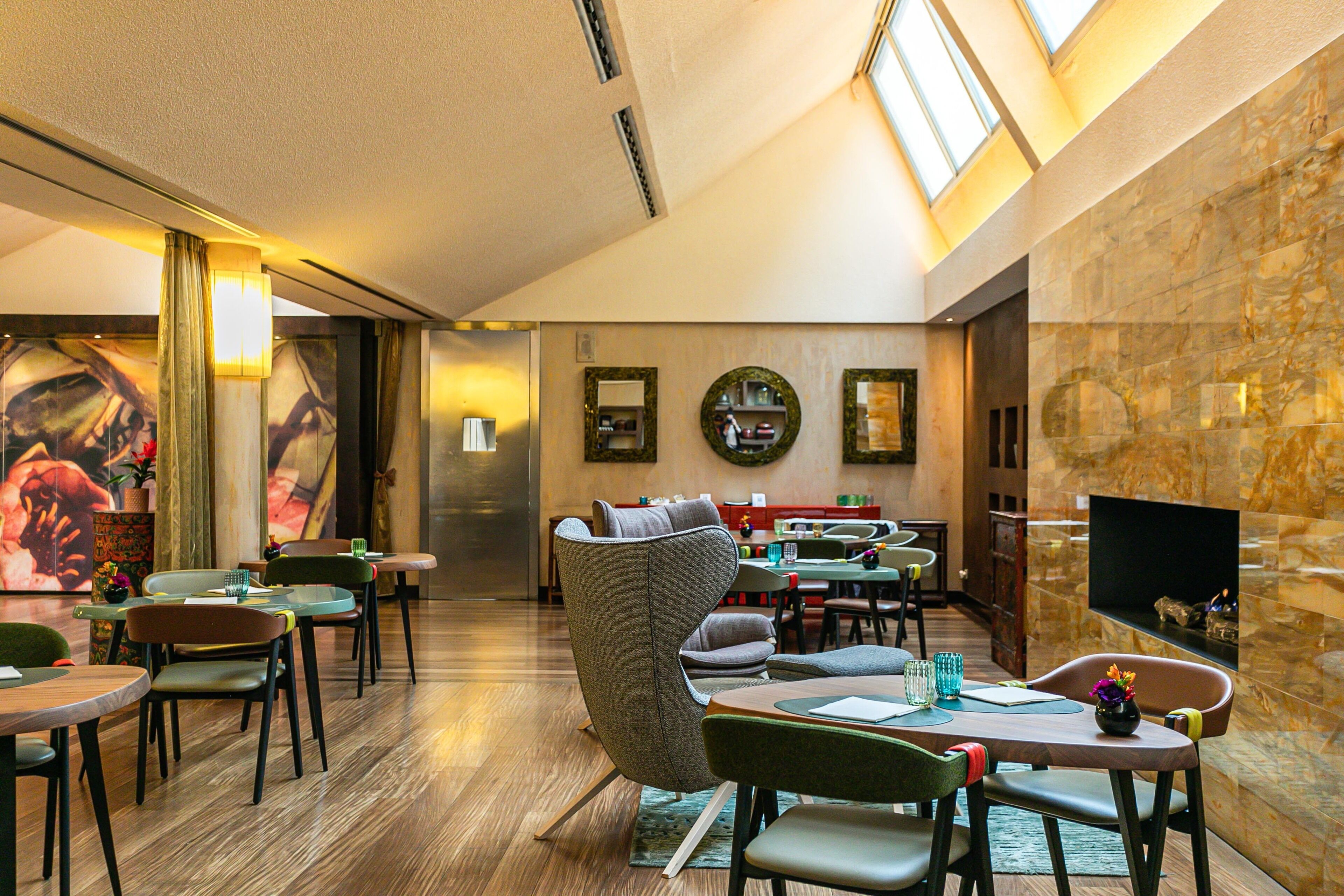 A modern hotel lobby with a high ceiling, a flat-screen TV, and a seating area with tables and chairs.