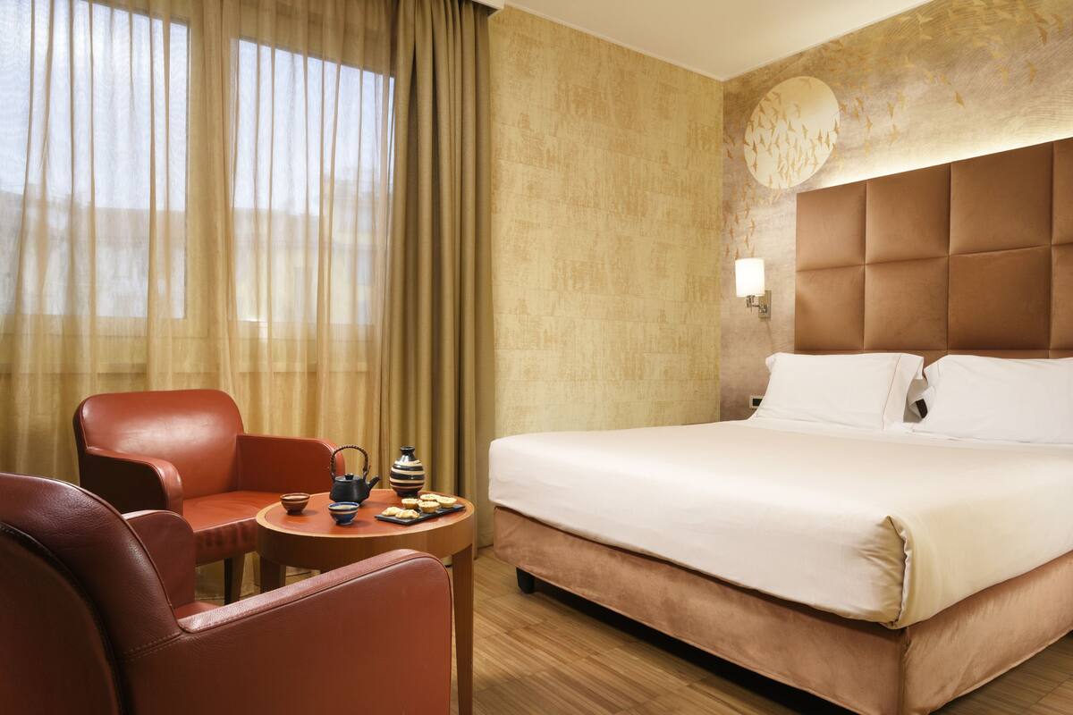 A hotel room with a large bed, a seating area with a table, and a window with curtains.