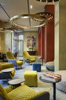 A modern lounge area with circular seating, a glass elevator, and abstract wall art.