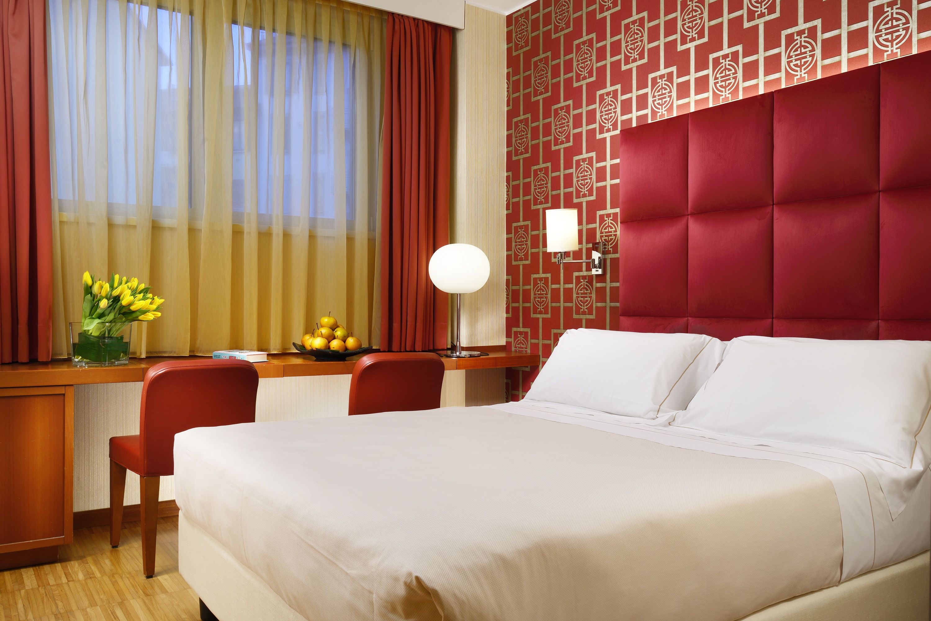 Een hotelkamer met een groot bed, een bureau met stoel, een lamp en een vaas met bloemen.