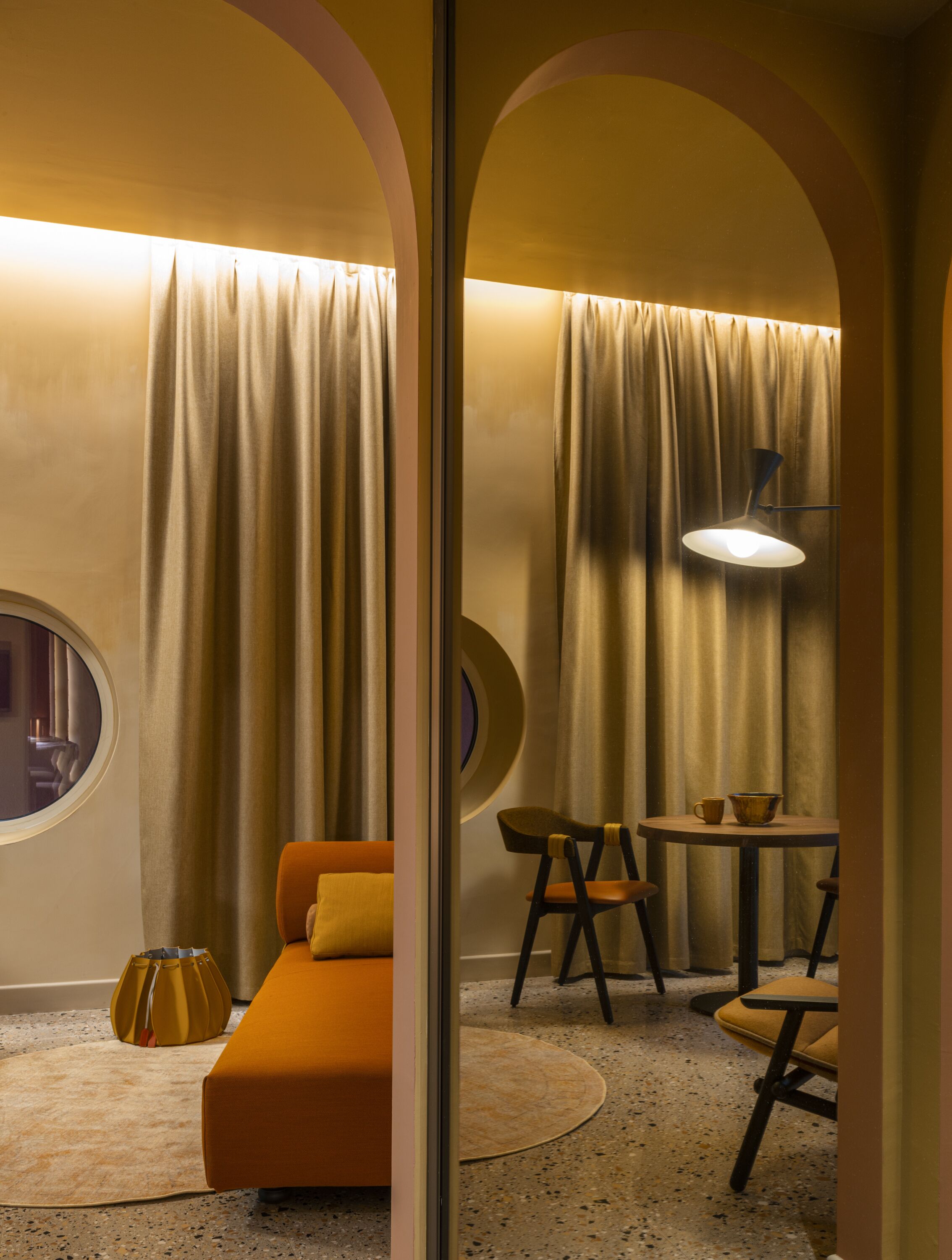 A cozy room with a round window, a sofa, a table with chairs, and a lamp.
