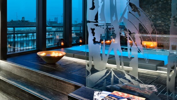 Un baño moderno con un ventanal grande, un separador de vidrio decorativo y un cuenco de velas.