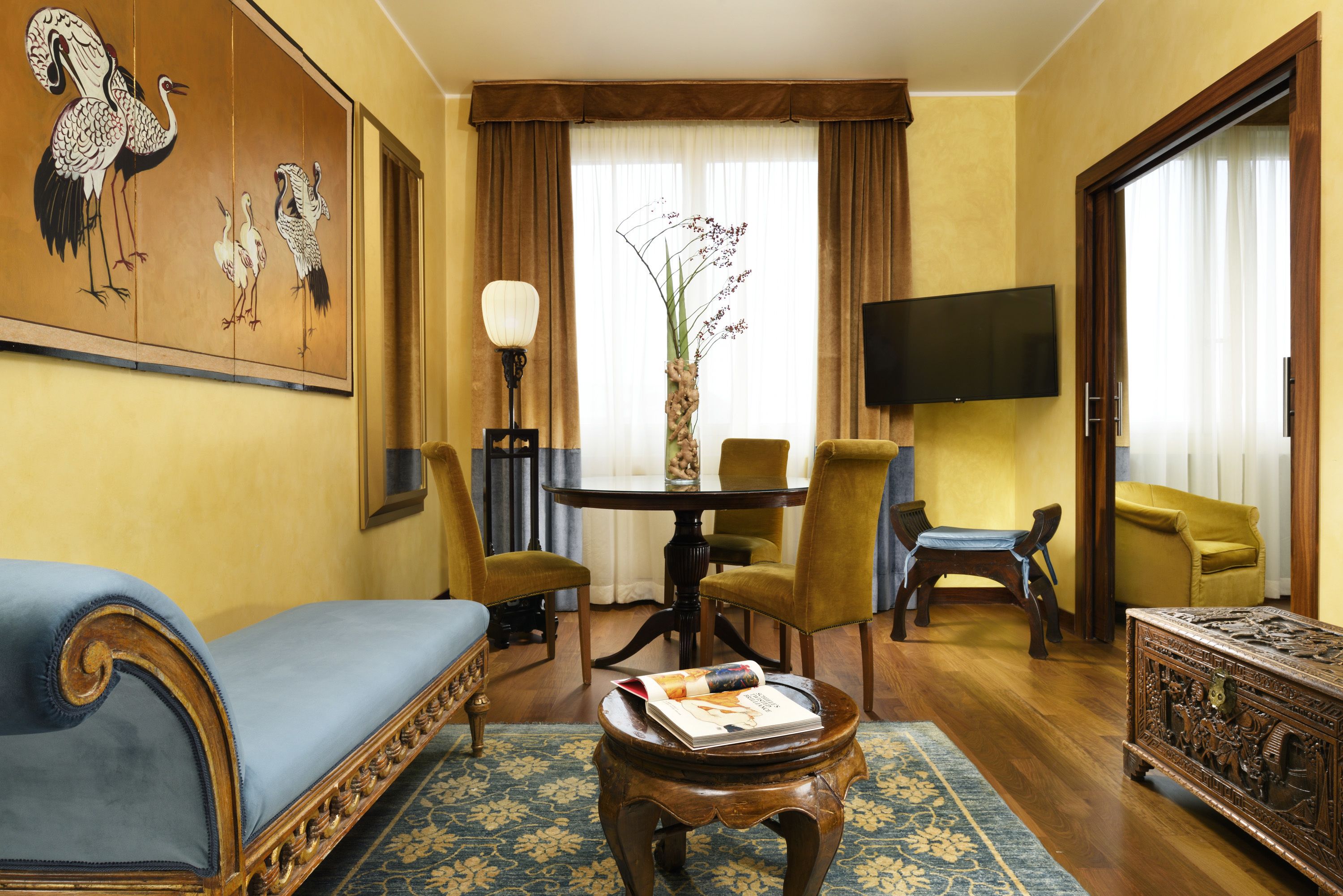 Un salon comprenant un canapé, des fauteuils, une table basse, un tableau, un téléviseur et une grande fenêtre avec des rideaux.