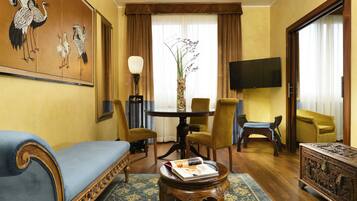 Un salon comprenant un canapé, des fauteuils, une table basse, un tableau, un téléviseur et une grande fenêtre avec des rideaux.