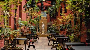 Un patio interior con mesas y sillas, una estatua y plantas en macetas.