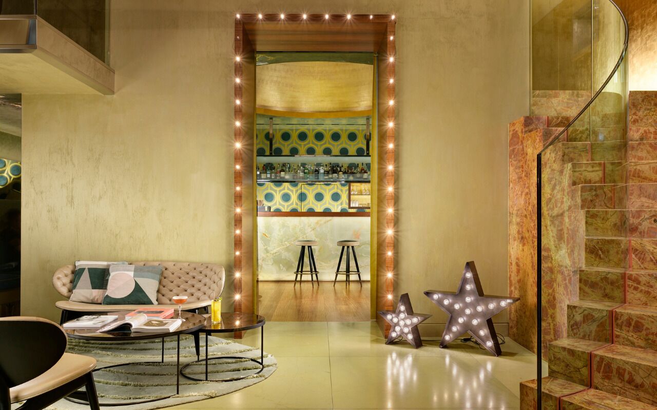 A room with a sofa, a bar area with stools, a star-shaped light fixture, and a staircase.