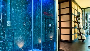 Un área de spa con paredes de vidrio, una bañera, una escalera de madera y piso de baldosas.