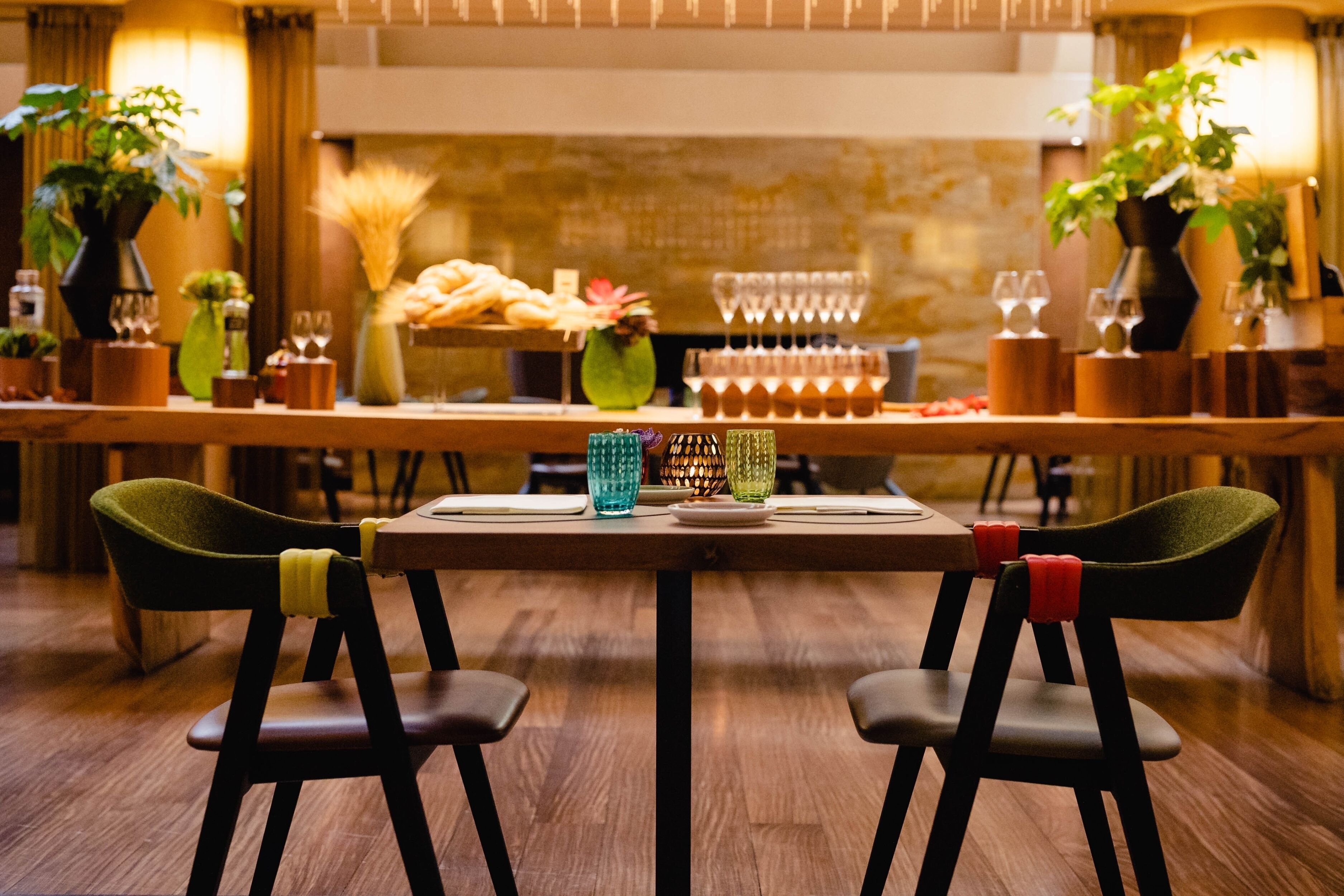 En restaurang med ett långt träbord, två gröna stolar och ett varierat utbud av rätter och drycker på bordet.