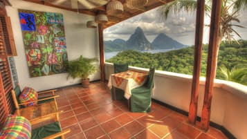 Un balcon avec une table et des chaises, un tableau accroché au mur et une vue sur une montagne et une forêt.