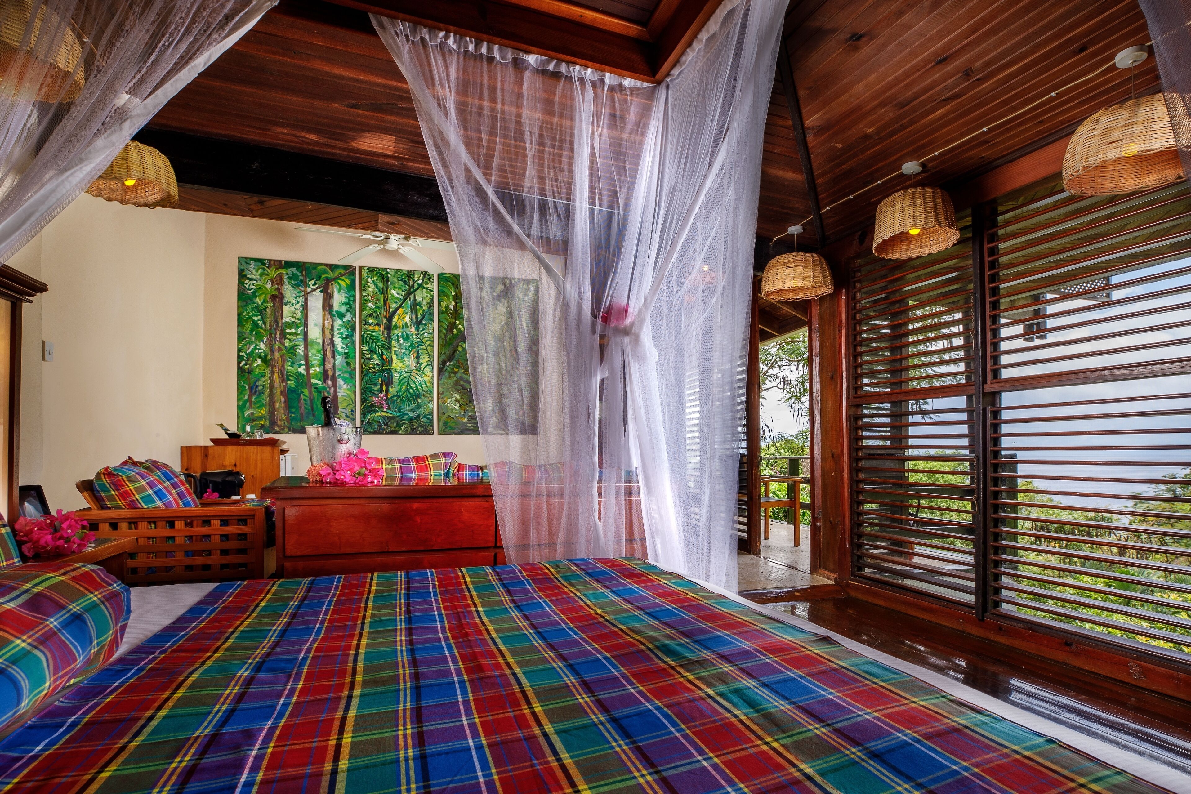 A bedroom with a plaid bedspread, wooden furniture, a red sofa, and a large window with blinds.