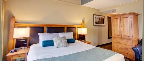 A hotel room with a large bed, two bedside tables with lamps, a wooden wardrobe, and a framed picture on the wall.