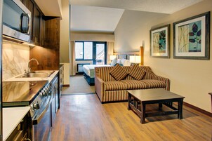 Una habitación de hotel compacta con kitchenette, un sofá, una mesita de centro y dos obras de arte enmarcadas en la pared.