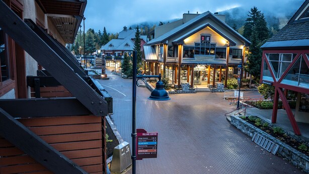 A building with a brick pathway leading to a well-lit entrance, a signboard, and a metal structure to the right. - Blackcomb Lodge (Whistler)
