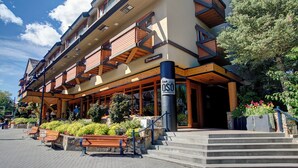 A hotel with a wooden facade, outdoor seating, and a staircase leading to the entrance. - Blackcomb Lodge (Whistler)