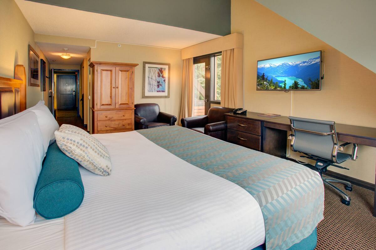 Habitación de hotel con una cama grande, un escritorio, una silla y un televisor en la pared.