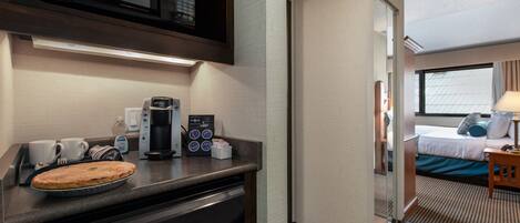 A compact hotel room with a kitchenette, a bed, and a view of the city.